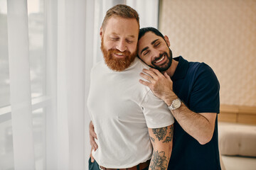 Two men hug each other warmly in front of a window in a modern living room, showcasing their love and connection.