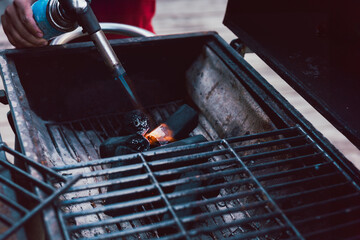 Man using BBQ lighter torch to start fire for charcoal.