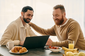 Two men immersed in a laptop screen at a table in a modern setting, engaged in a shared activity.