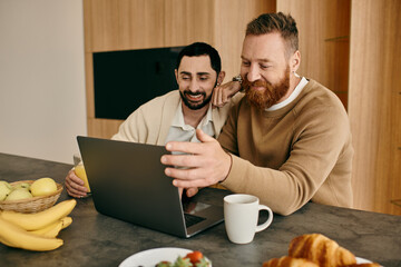 Two men immersed in work, sitting at a table and sharing a laptop in a cozy, modern apartment.