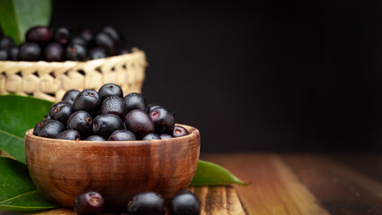 A wooden bowl filled with 'Indian blackberry' or Jamun (Syzygium cumini) fresh fruits, on a dark...