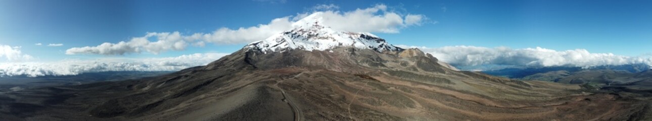 Chimborazo Volcano snowcapped peak with small clouds and road leading up to the volcano.