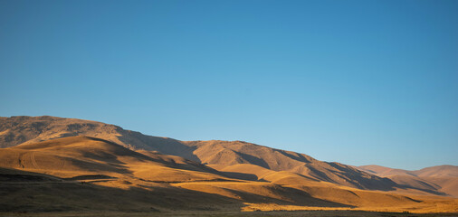 a vast, open landscape at golden hour with rolling hills, a clear sky, and the play of shadows and light creating a tranquil, picturesque scene
