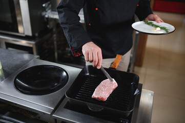 Chef in hotel or restaurant kitchen cooking, he is cutting meat or steak