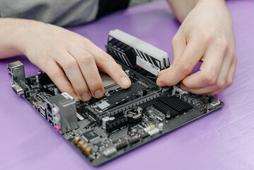 system administrator installing SSD into motherboard, assembling PC of different accessories or components, close-up view of hands, computer repair and maintenance concept