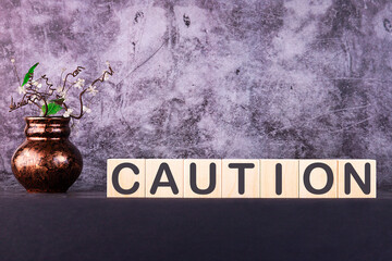 Word CAUTION made with wood building blocks on a gray background