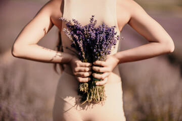 girl holding bouquet lavender flowers. The flowers are purple and the woman is wearing a tan top....