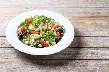 Healthy chickpea salad with tomato,lettuce and cucumber on wooden table. Copy space