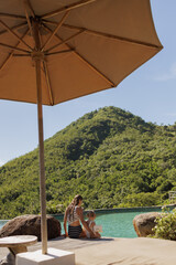 Back view woman and her child sitting by the pool under umbrella, Healthy travel lifestyle, kids on...