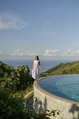 Romantic girl in long white dress enjoying rest at exotic resort. with nature and ocean view...