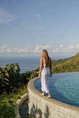 A beautiful girl  wearing long white dress a by the pool in the morning in Bali, Indonesia. Young...