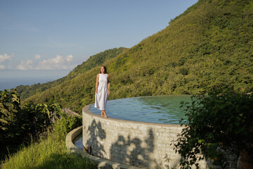 Happy woman enjoying  tropical vacation near infinity pool with a jungle  sea view in  Bali. Young...