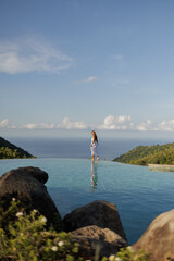 Asian woman in white dress walk on the edge of infinity pool above the sea with nature view. Young...