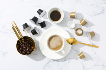 Coffee capsules and beans, cups with coffee drink on marble background, top view