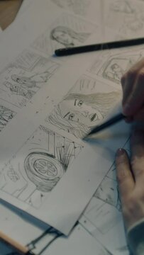 Young female artist draws sketches of comic book characters on a sheet of paper. The illustrator creates a storyboard. Storytelling concept. Video editing. Vertical shot.