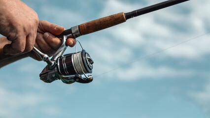 Freshwater fishing in summer. Spinning reel on a spinning rod in the hands of a fisherman.