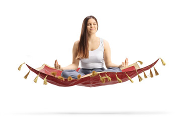 Young female in pajamas sitting on a flying carpet and meditating