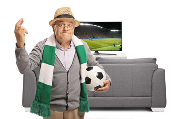 Elderly fan with a football and a scarf holding his fingers crossed for luck for the football match...