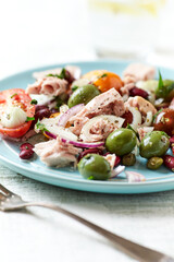 Salad with tuna, green olives and cherry tomatoes. Bright wooden background. Close up. Copy space.
