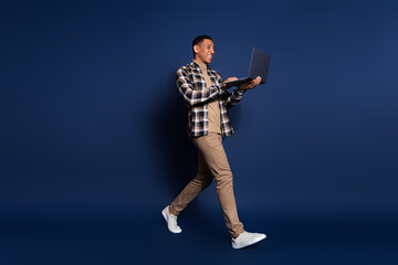Photo of handsome good mood guy wear checkered shirt walking typing modern gadget isolated blue color background