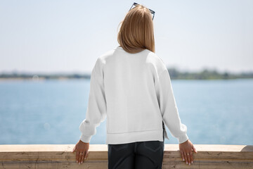 White sweatshirt template with side slits on girl, back view, lady on quay, blurred river...