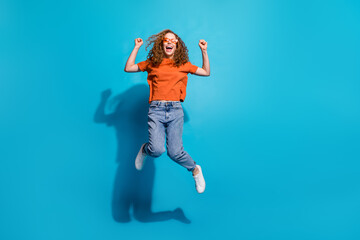 Photo of positive cheerful girl jump up raise fists winning isolated blue color background