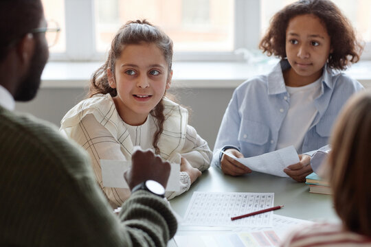 Over-the-shoulder shot of kids sitting at table listening to teacher and looking at cards he showing to them