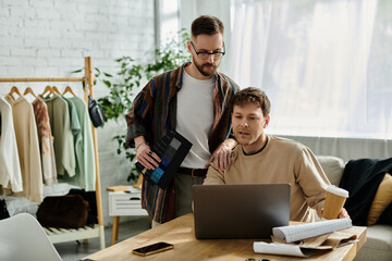 Two men, partners in design, discuss ideas over a laptop in a stylish clothing store.