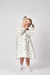 Portrait of cute little girl on a white background. Full length standing and smiling little girl, wearing white dress looking at camera