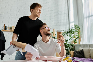 Two men, a gay couple, sit at a table in a designer workshop, passionately creating trendy attire.