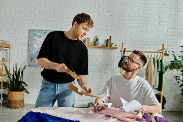 Two men, a gay couple, work together in a designer workshop cutting a piece of paper for their...