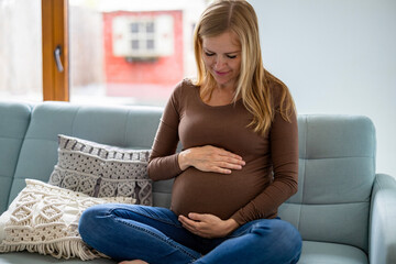 Pregnant woman touching her belly, relaxing on sofa at home
