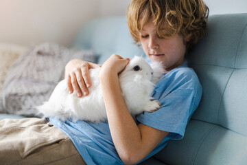 Cute little boy cuddling his bunny pet at home
