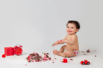 Cheerful cute kid laughing next to his messy first birthday cake 