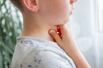 close-up neck, caucasian child patient holding affected area, experiencing throat pain, loss of...