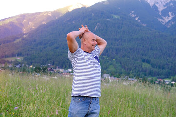 mature man, senior 60 years old standing in mountains above city, smiles, Alps are behind him,...