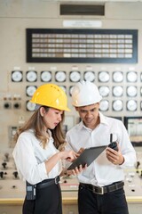 Two Asian engineers, within the industrial sector, work in tandem at the power plant, their laptops...