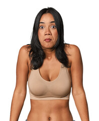 Fototapeta premium Young Filipino woman in light wear shrugs shoulders and open eyes confused.