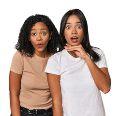 Young Latin friends in studio praying for luck, amazed and opening mouth looking to front.