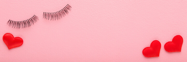 Red heart shapes and dark black false lashes on light pink table background. Pastel color. Closeup. Wide banner. Empty place for text. Top down view.