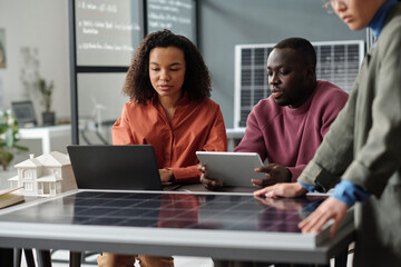 Two young African American employees with laptop and tablet preparing new business project while sitting by workplace in office