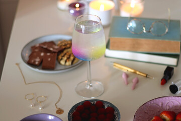 Plate of pastel macarons, cookies and chocolate, cup of tea of coffee, glass of bubble water, various berries, books and accessories on the table. Selective focus, pastel colors.