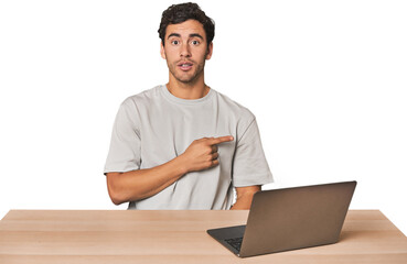 Hispanic young man working on laptop pointing to the side