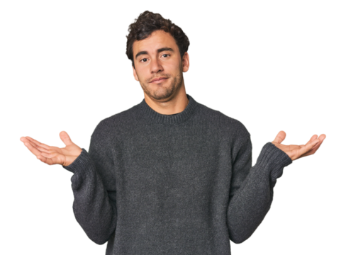 Young Hispanic man in studio doubting and shrugging shoulders in questioning gesture.