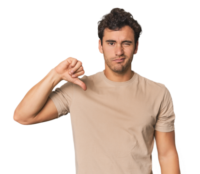 Young Hispanic man in studio showing thumb down, disappointment concept.
