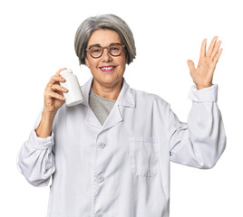 Caucasian mid-age pharmacist with pill bottle receiving a pleasant surprise, excited and raising hands.