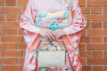 Naklejka premium 成人式、紅葉を背景にした振袖の女性の手元とバッグ