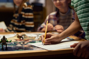 Hands of youngster pointing at paper with board game rules and ticking them while distributing roles among his friends before playing