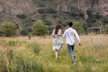A couple running in a field with a cloudy sky in the background. Scene is romantic and adventurous