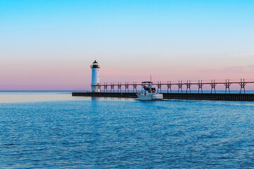 Boat moving down a channel next to a pier and lighthouse